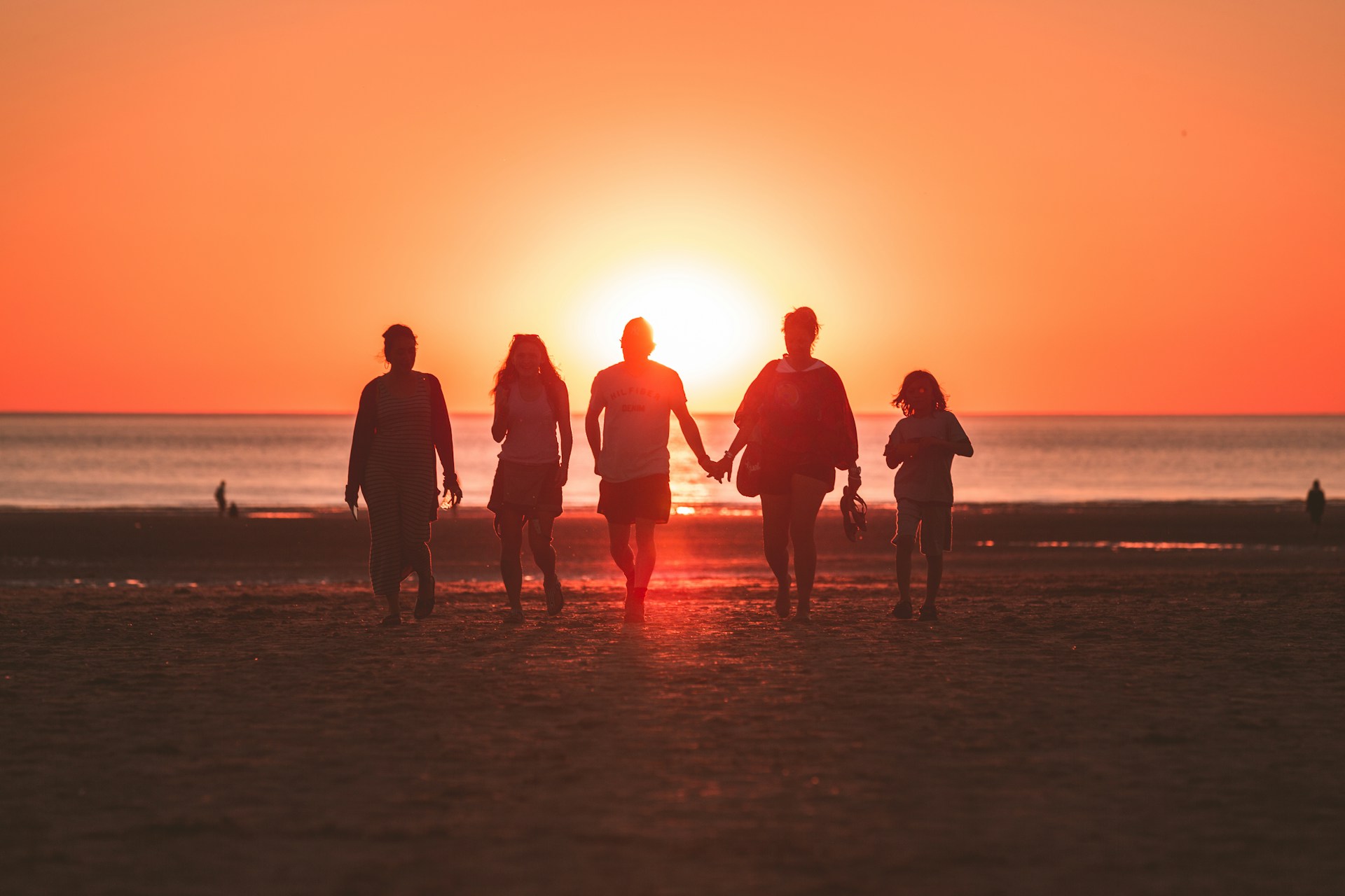 Fotografía a color de una familia al atardecer en la playa a contraluz del sol