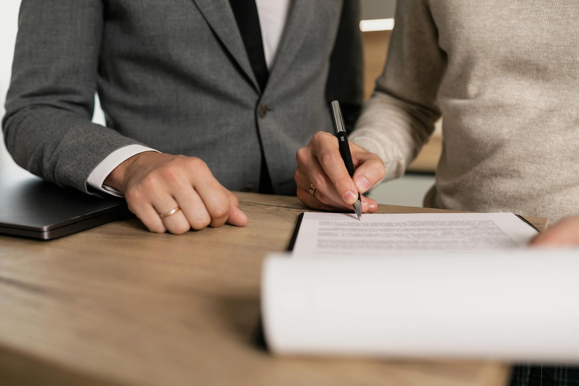 Fotografía a color de una persona firmando un contrato delante de un hombre en traje chaqueta