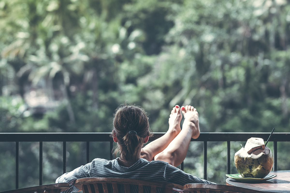 Fotografía a color de una mujer sentada relajada en una terraza delante de unos árboles